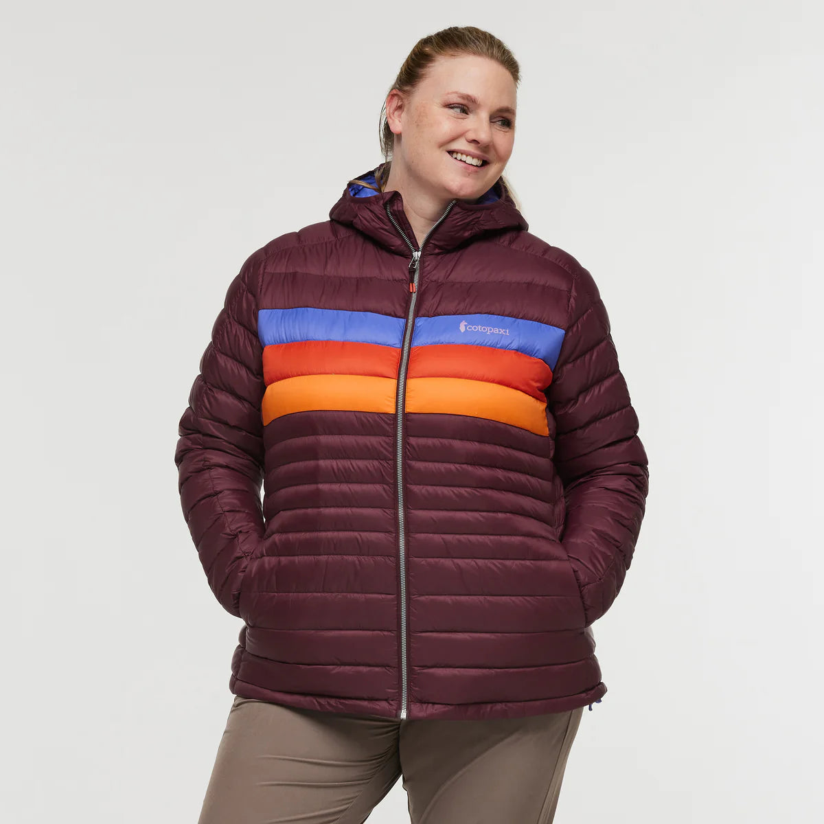 Plus size woman wearing Cotopaxi Fuego Down Plus Size Hooded Jacket in Wine Stripe