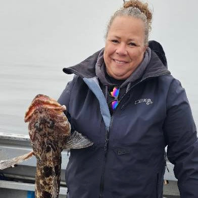 Plus Size Woman fishing in Alaska holdiong a fish she just caught.