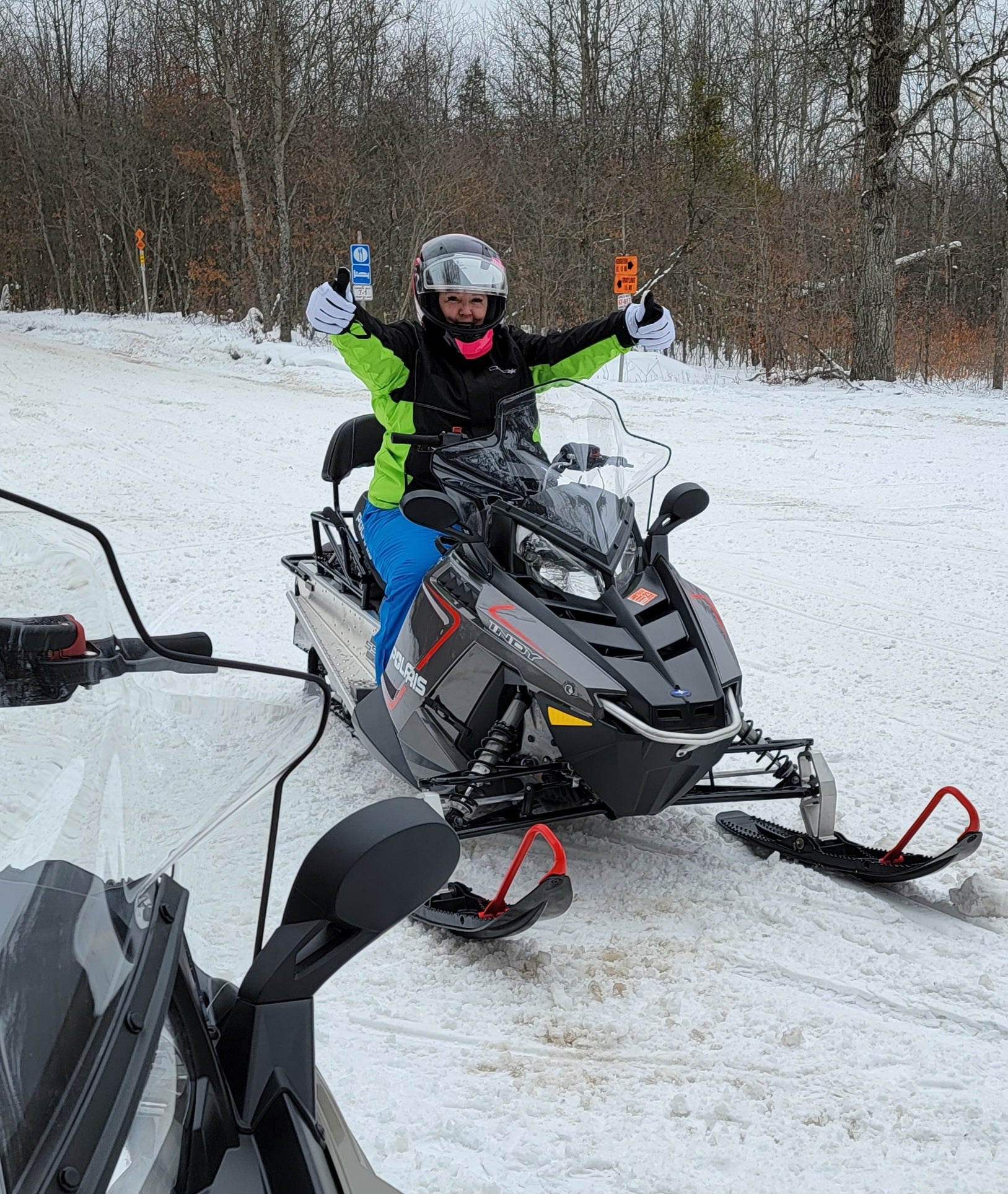 Plus Size woman on a snowmobile, giving the thumbs up and smiling.