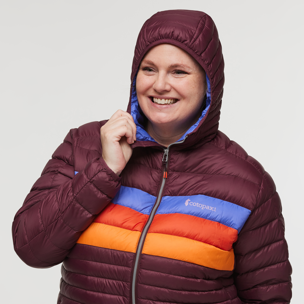 View of plus size woman with hood up wearing Cotopaxi Fuego Down Plus Size Hooded Jacket in Wine Stripes